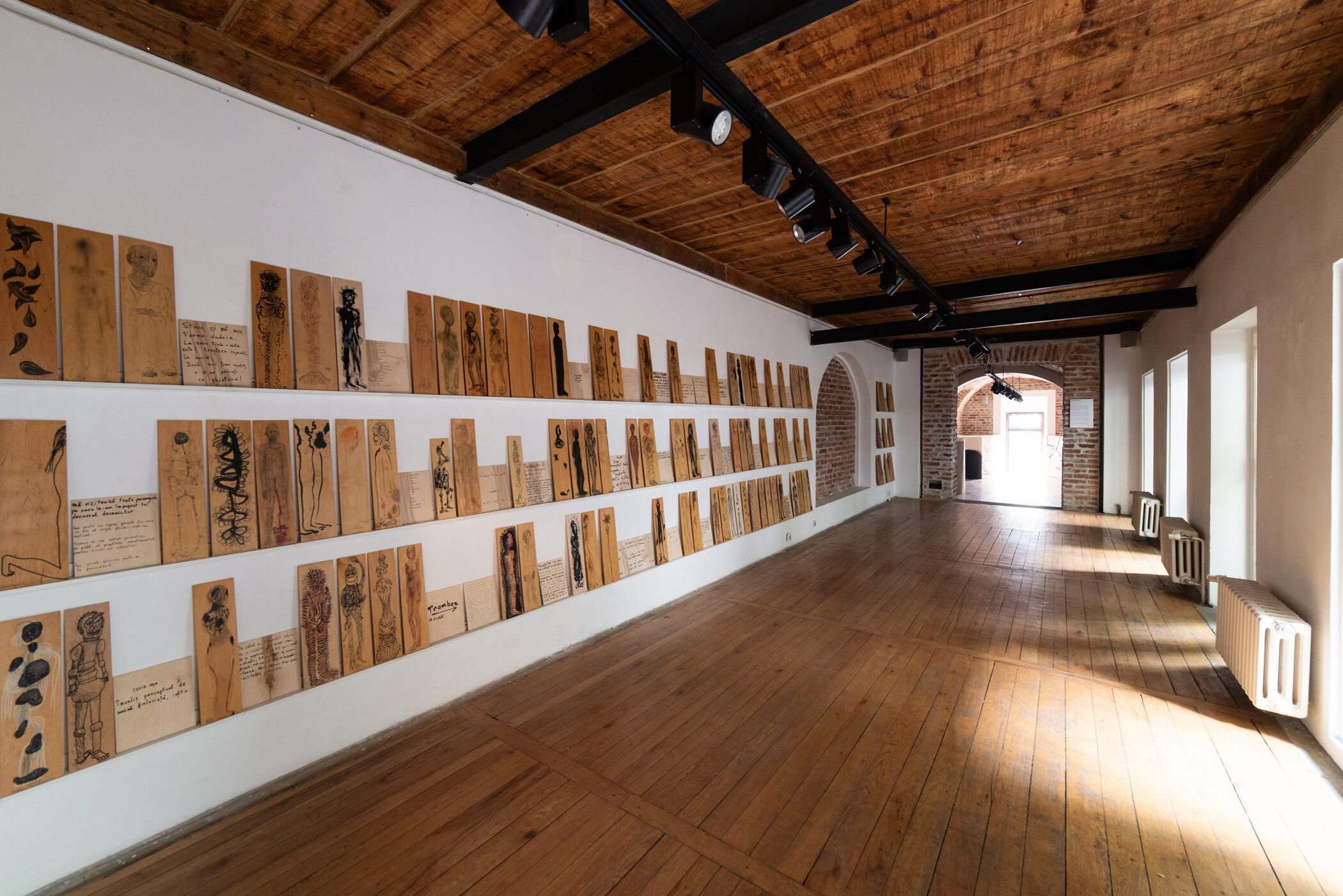 Setki wąskich rysunków ustawionych na ścianach galerii